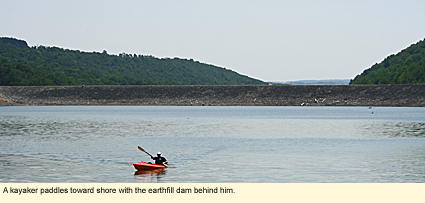 A kayaker paddles toward shore with the earthfill dam behind him at Almond Lake near Hornell, New York.