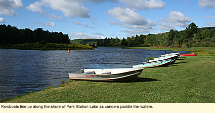 Rowboats line up along the shore of Park Station Lake as canoers paddle the waters.