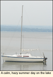 An anchored sailboat at rest on a calm, hazy summer day on Cayuga Lake in the Finger Lakes, New York USA.