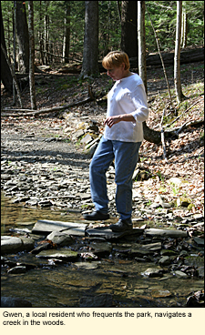 Gwen, a local resident who frequents the park, navigates a creek in the woods at Tow Rivers State Park in Waverly, New York, USA.